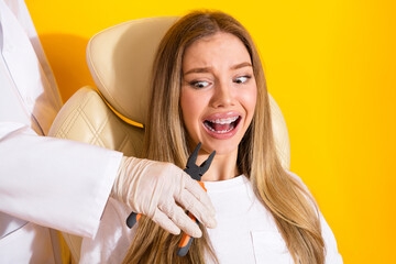 Dental checkup scene with young woman braces smiling in dental chair against yellow background