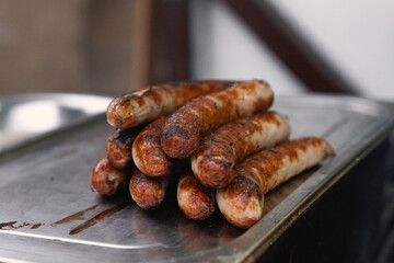 Delicious Grilled Sausages Stacked Neatly on a Silver Tray at a Festive Christmas Market, Surrounded by Joyful Holiday Atmosphere and Twinkling Lights