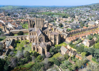 Aerial view of the magnificent Wells Cathedral standing proud amidst a tapestry of terracotta rooftops and verdant trees under a clear sky, Wells, Somerset, England.