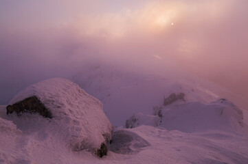 Aerial view of snow-laden rocks and peaks shrouded in a soft, ethereal mist, kissed by the pale glow of the sun, Konske, Zilina Region, Slovakia.