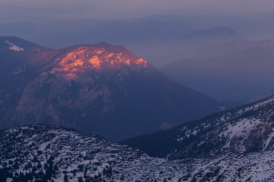 Aerial view of the mountain tops kissed by the warm glow of the setting sun, casting shadows across the snow-dusted peaks, Konske, Zilina Region, Slovakia.