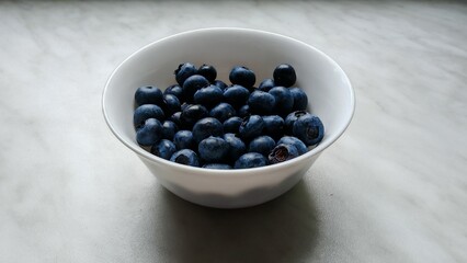There is a ceramic bowl with delicious, healthy and vitamin-rich blueberries on the table