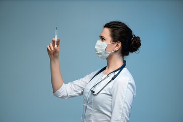 Side view nurse holding syringe upright preparing injection while wearing mask in clinical setting