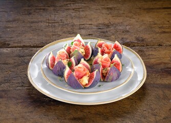 Fresh figs are artistically arranged on a decorative plate. They are garnished with creamy cheese and rosy prosciutto, creating a delectable appetizer