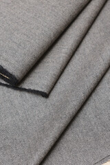 Close-up view of classic English tweed wool fabric in a fine gray and black herringbone weave. Detailed texture and folded pattern perfect for tailoring suits, coats, and blazers.