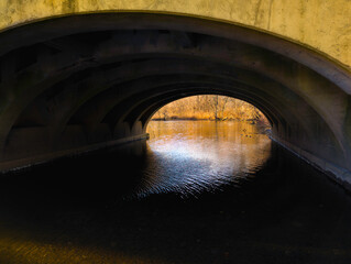 Naklejka premium Sunrise glows beneath the arching bridge over Mill River in East Rock Park, New Haven, Connecticut, United States, an abstract geometry of architecture, light, shadow, and water reflection.