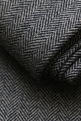 Close-up view of classic English tweed wool fabric in a fine gray and black herringbone weave. Detailed texture and folded pattern perfect for tailoring suits, coats, and blazers.