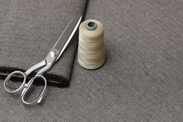 Close-up of tailoring scissors and a spool of beige thread resting on a folded piece of gray and...