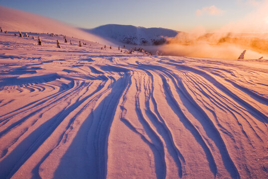 View of snow-covered landscape with wind-sculpted patterns under a sky ablaze with pastel hues, creating a tranquil winter scene, Velka Hola, Banska Bystrica Region, Slovakia.