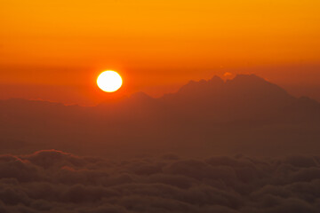 Aerial view of the sun setting, casting a warm glow over the mountains and clouds, creating a serene and majestic scene, Triglavski narodni park, Gorenjska, Slovenia.