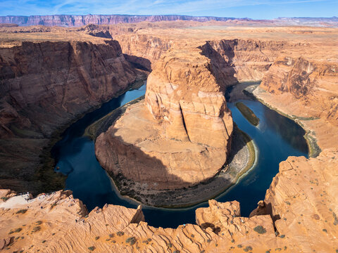 Aerial view of the powerful Colorado River carves through the ochre-red sandstone of Horseshoe Bend, creating a striking contrast of textures and tones, Page, Arizona, USA.