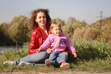 Fototapeta premium A woman and a child are sitting on the grass. The woman is wearing a red jacket and the child is wearing a pink jacket. Scene is warm and friendly, as the woman