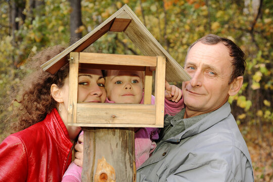 A man and a woman are holding a child in front of a bird feeder. Scene is warm and loving - Powered by Adobe
