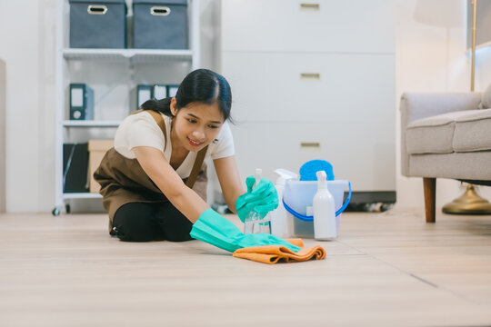 An Asian woman housekeeper wearing gloves and an apron is cleaning a modern office or home. She works diligently, maintaining hygiene and order as part of professional cleaning service - Powered by Adobe