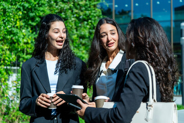 Three businesswomen talking and drinking coffee outdoors, showcasing teamwork, communication, and professional collaboration in a modern corporate environment. Ideal for business, leadership, and work