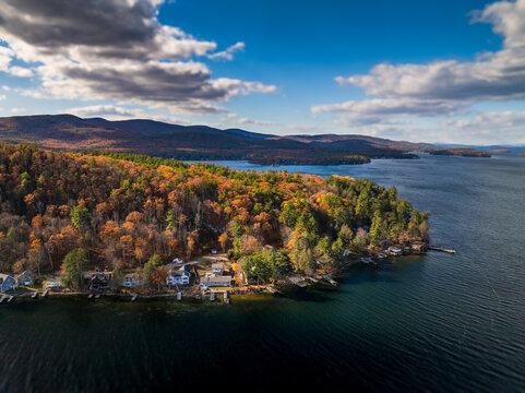 Aerial view of autumn's fiery hues paint the forest bordering the tranquil lake, a serene landscape under a crisp blue sky, Alton, New Hampshire, United States.