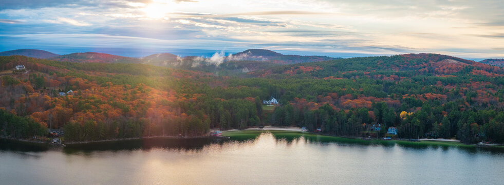 Aerial view of a serene lake reflecting the vibrant autumn foliage under a hazy sky, Alton, New Hampshire, United States.