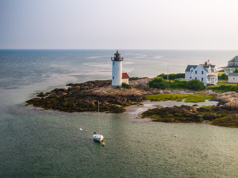 Aerial view of the historic white lighthouse standing proudly against the rocky shore, adjacent to a quaint white house, kissed by the ocean's edge, Gloucester, Massachusetts, United States.
