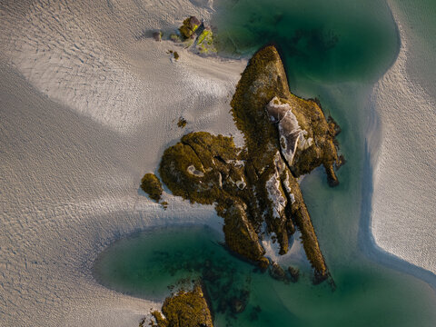 Aerial view of the stark contrast between the rugged, moss-covered rocks and the soft, rippled sand, with pools of turquoise water creating a serene scene, Gloucester, Massachusetts, United States.