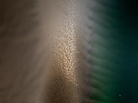 Aerial view of the meeting point of sandy textures and the dark, rippling ocean, creating a mesmerizing contrast of earth and sea, Gloucester, Massachusetts, United States.