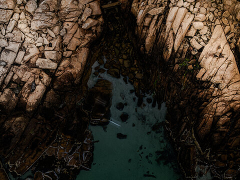 Aerial view of rugged, sun-kissed rocks embrace a hidden pool of emerald water, creating a dramatic contrast of textures and tones, Gloucester, Massachusetts, United States.