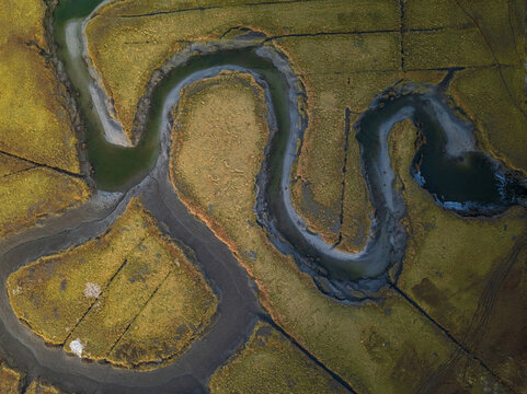 Aerial view of a serpentine river twisting through a patchwork of golden marshes, creating a mesmerizing dance of light and shadow, Gloucester, Massachusetts, United States.