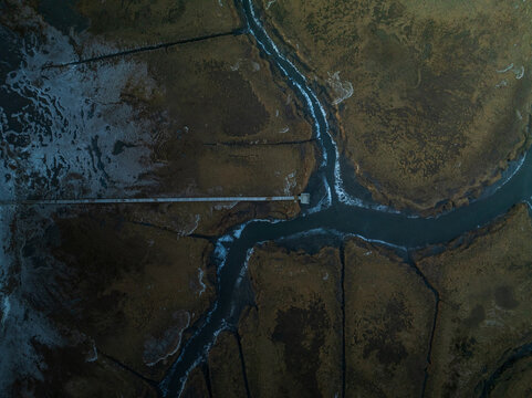 Aerial view of winding waterways carve through the dark, textured marshlands, creating a mesmerizing contrast of light and shadow, Gloucester, Massachusetts, United States.