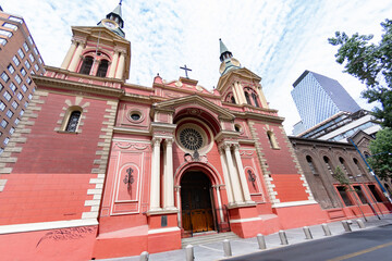 View of the vibrant red facade of Iglesia de los Sacramentinos stands in stark contrast to the modern glass skyscraper, Santiago, Chile.
