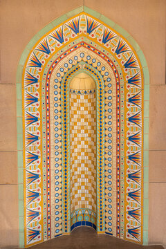 View of an arched niche with intricate geometric patterns in shades of gold, blue, and green on a textured wall, Muscat, Muscat Governorate, Oman.
