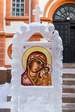 View of a religious icon framed in ice stands serenely before a church with orange trim, contrasting sharply with the crisp white snow, Irkutsk, Irkutsk Oblast, Russia.