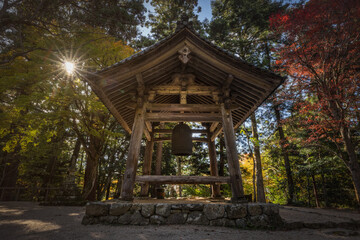 View of the wooden bell tower stands serene against a backdrop of colorful autumn foliage, bathed in the golden light of the setting sun, Kyoto, Kyoto, Japan.
