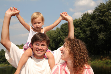 A family of three, a man, a woman and a child, are smiling and enjoying a day outdoors