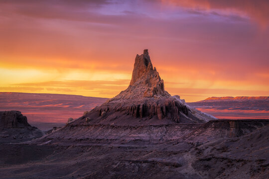 View of a stark, rocky mesa highlighted by a fiery sunset casting long shadows across the arid landscape, its peak piercing the vibrant sky, Aktau, Mangystau Region, Kazakhstan.