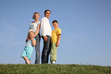 Fototapeta premium A family of four is standing on a grassy hill, with the father and mother standing between the two children