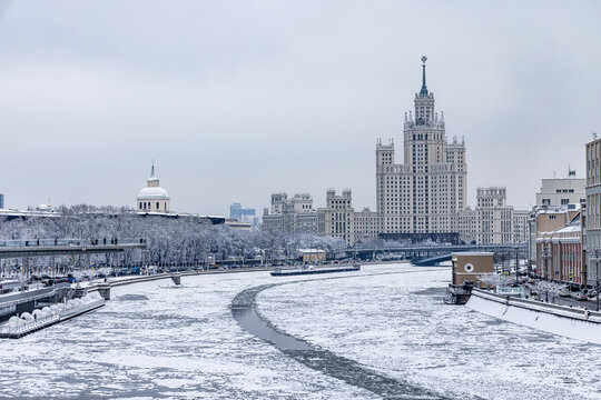 View of a wintry scene unfolds with a river cutting through a snow-dusted cityscape dominated by a towering Stalinist skyscraper, Moscow, Moscow, Russia.