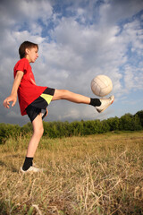 Naklejka premium A boy kicks a soccer ball in a field. The sky is cloudy and the grass is dry