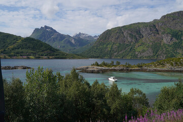 Beautiful aerial view of the harbour at Lofoten islands with green transparent water, small boat on the foreground and snowy mountains on the background.