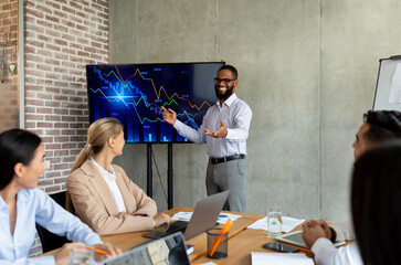 A businessman shares company growth insights during a meeting with coworkers in a contemporary office. Colleagues engage with financial performance data displayed on a monitor.