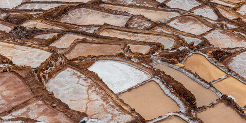 Maras, Cusco, Peru: geometric salt ponds forming abstract mineral patterns in the Andes mountains. Fine art landscape with earthy tones and natural texture harmony.