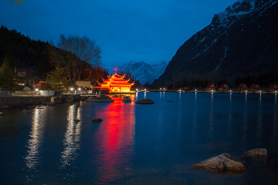 View of illuminated pagoda-style structure reflecting vibrantly on the serene lake under the dark blue sky, flanked by mountains, Kachora, Gilgit Baltistan, Pakistan.