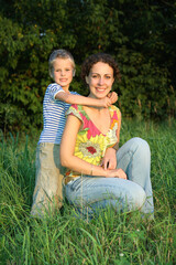 Fototapeta premium A woman and a child are sitting in a grassy field. The woman is wearing a yellow shirt and blue jeans. Scene is happy and relaxed