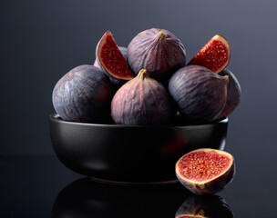 Ripe fig fruit in black dish on a black reflective background.