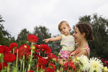 A woman and a child are sitting in a field of red flowers. The woman is pointing at something in the distance