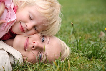 A woman and a child are laying on the grass. The woman is smiling and the child is smiling. Scene is happy and peaceful