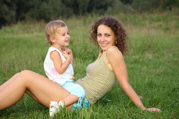 Fototapeta premium A woman and a child are sitting on the grass. The woman is smiling and the child is laughing