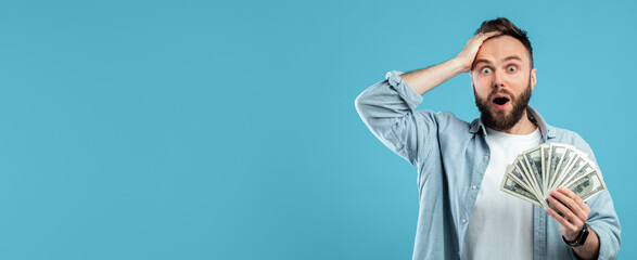 A man with a beard looks shocked while holding stacks of money. He shows a surprised expression...
