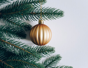 Golden Christmas Ornament Hanging on Lush Green Pine Branches Against a Clean White Background in Minimalist Holiday Still Life Photography