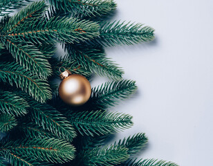 Golden Christmas Ornament Hanging on Lush Green Pine Branches Against a Clean White Background in Minimalist Holiday Still Life Photography