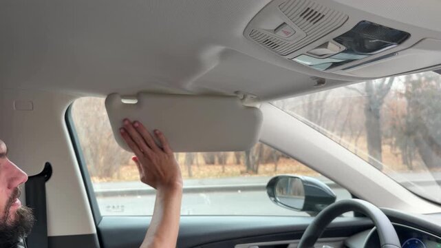 Close-up of a driver's hand pulling down the car's sun visor to block bright light or sun glare. Modern vehicle interior detail showing a safety feature activated by the person driving.