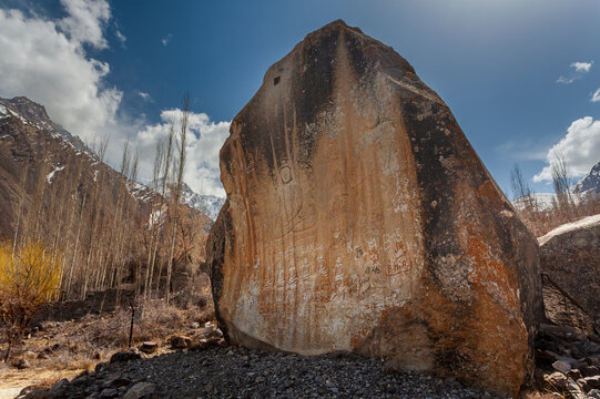 View of a massive, weathered rock monolith standing sentinel against a backdrop of stark, snow-dusted mountains and spindly trees, Skardu, Gilgit Baltistan, Pakistan.